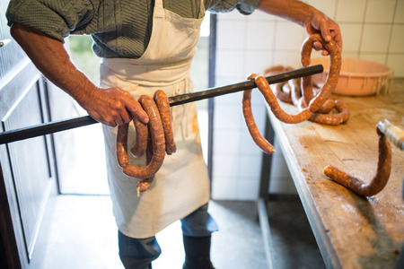Unrecognizable man hanging homemade raw sausages on wooden stick, making them the traditional way. Close up.の写真素材