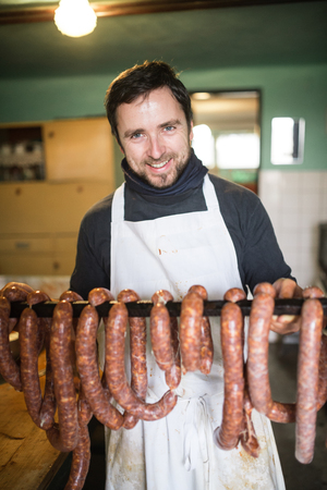Man hanging homemade raw sausages on wooden stick, making them the traditional way. Close up.の写真素材