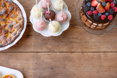 Table with naked cake decorated with chocolate and fruit, sweet pie and colorful cakepops. Studio shot on brown wooden background. Copy space. Flat lay.の写真素材