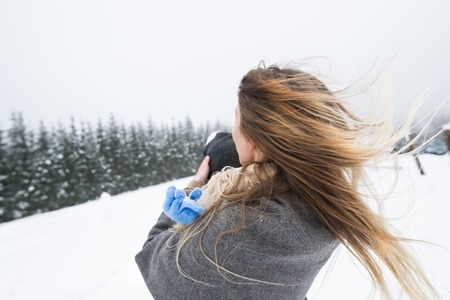 Beautiful young mother outside having fun with her son, playing in the snow. Foggy white winter nature. Rear view.の写真素材