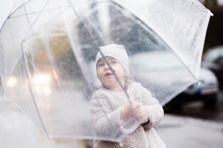 Cute little girl under the transparent umbrella in town on a rainy day.の写真素材