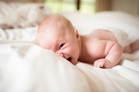 Close up of cute little baby boy lying on bed making funny face, laughing.