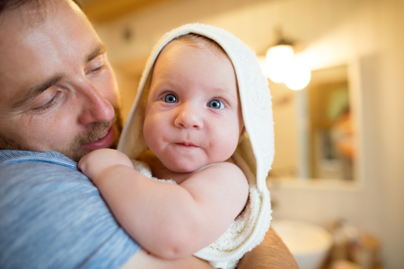 Young father holding in his arms his son wrapped in towel after bathing him. Close up.の写真素材