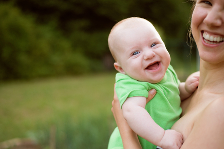 Close up of beautiful young mother holding her baby son, laughing. Sunny summer nature.の写真素材
