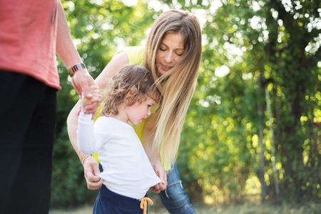 Cute little boy with his beautiful mother and unrecognizable father in green sunny summer nature.の写真素材