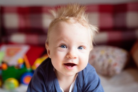 Close up of cute little baby boy with spiky blonde hair crawling on bed.