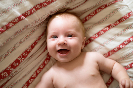 Close up cute little baby boy lying on bed. Red striped bedding with folk pattern.の写真素材