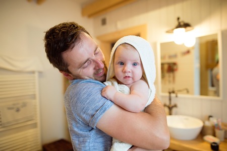 Young father holding in his arms his son wrapped in towel after bathing him. Close up.の写真素材