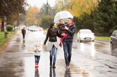 Beautiful young family with two daughters under the umbrellas. Walking in the street on a rainy day.の写真素材