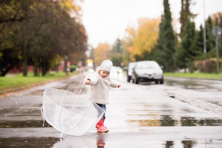 Cute little girl playing with transparent umbrella in town on a rainy day.の写真素材