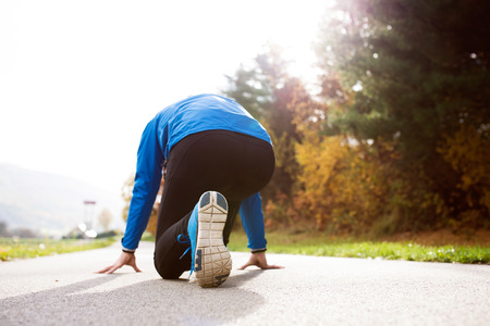 Young runner in blue jacket at the lake on an asphalt path leading through green grass in steady...