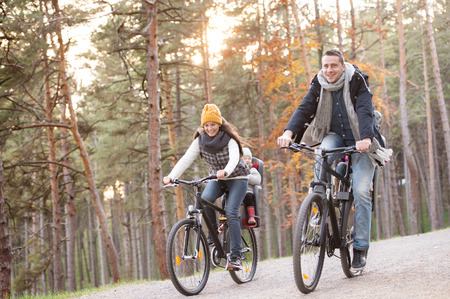 Beautiful young family with two daughters in bicycle seats in warm clothes cycling outside in autumn natureの写真素材