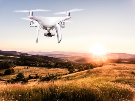 Close up of hovering drone taking pictures of green meadows and hills at sunset