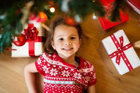 Beautiful little girl under Christmas tree lying among presents.の写真素材