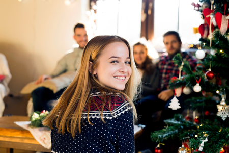 Young friends at decorated Christmas tree celebrating Christmas together. Teenage girl in sweater with nordic pattern smiling.の写真素材