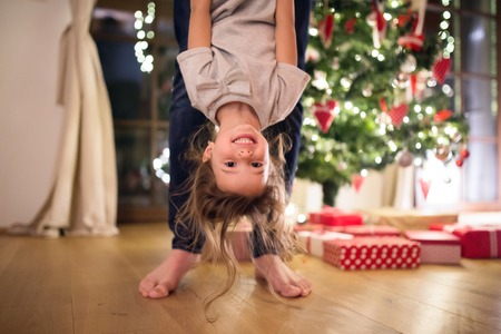 Unrecognizable young father with his little daughter at decorated Christmas tree together, holding her upside down.の写真素材
