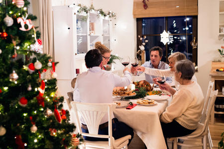 Beautiful big family sitting at the table, celebrating Christmat together at home. Illuminated Christmas tree behind them.の写真素材