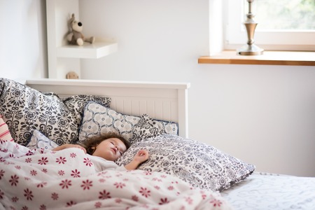 Cute little girl sleeping in the afternoon in bed, surrounded by pillows and bedding sheets.の写真素材