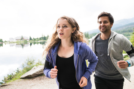 Beautiful young couple running on a path at the lake in green nature.の写真素材