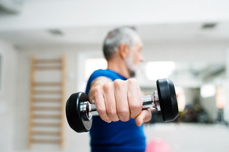 Senior man in sports clothing in gym working out with weights. Close up of hands.の写真素材