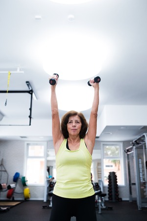Senior woman in gym working out with weights.