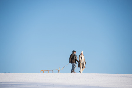 Beautiful senior couple on a walk pulling sledge, winter day.の写真素材