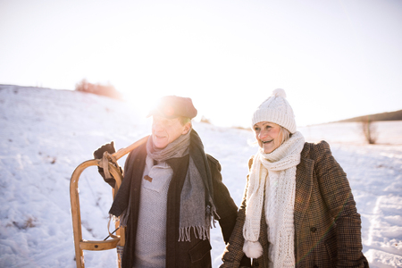 Beautiful senior couple carrying sled, sunny winter day.の写真素材