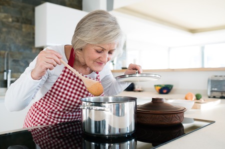 Senior woman in the kitchen cooking, mixing food in a pot.の写真素材