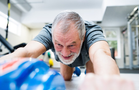Senior man in gym exercising abs with wheel rollerの写真素材