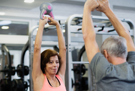 Senior couple in gym working out using kettlebells.の写真素材
