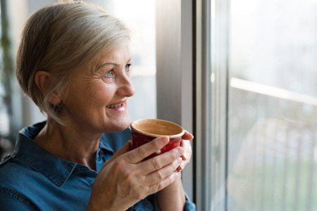 Senior woman at the window holding a cup of coffeeの写真素材