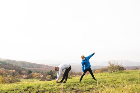 Two young hipster runners in sunny autumn nature stretching legs
