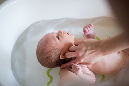 Unrecognizable mother bathing her son in white small plastic batの写真素材