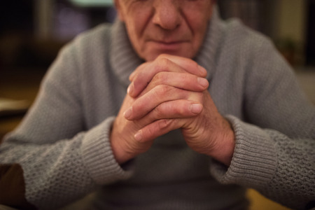 Unrecognizable senior man at home praying, hands clasped togetheの写真素材