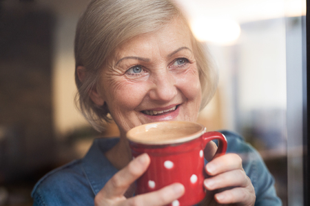 Senior woman at the window holding a cup of coffeeの写真素材