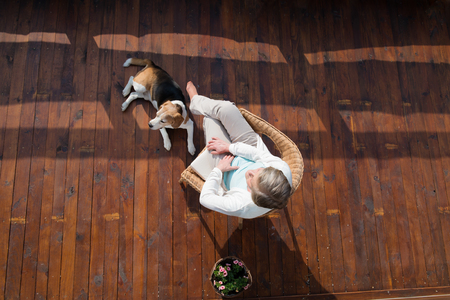 Senior woman with dog, sitting on wooden terrace, relaxing.の写真素材