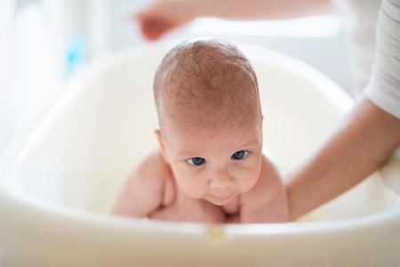 Unrecognizable mother bathing her son in white plastic bath
