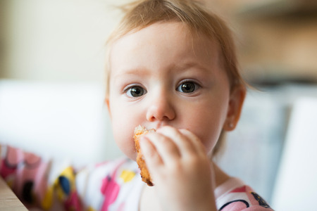 Cute little girl sitting at the table eating croissantの写真素材