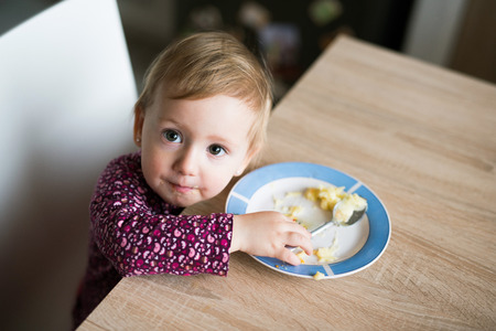 Cute little girl sitting at the table eating mashed potatoesの写真素材