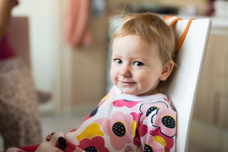 Cute little girl in the kitchen sitting on chair, smilingの写真素材
