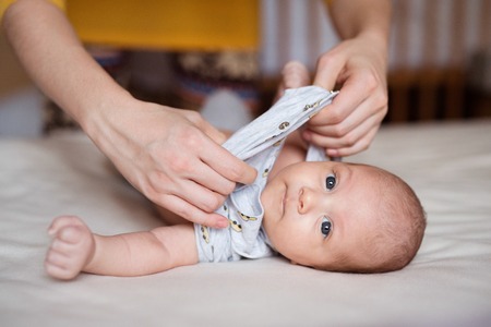Mother dressing her newborn baby son lying on bedの写真素材