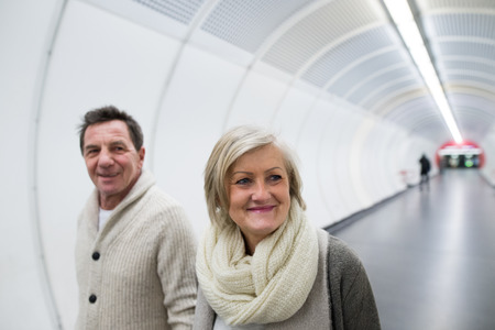 Senior couple in winter clothes walking in hallway of subwayの写真素材