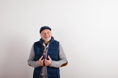 Senior man in sweater, vest jacket and cap, studio shot.の写真素材