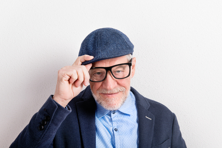 Senior man in blue shirt, jacket, eyeglasses and cap, studio shoの写真素材