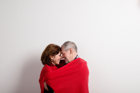 Senior couple hugging, wrapped in red blanket. Studio shot.の写真素材