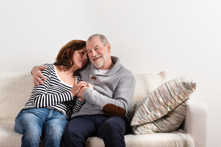 Beautiful senior couple sitting on couch, hugging. Studio shot.の写真素材