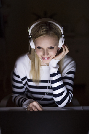 Woman sitting at desk and working on laptop at night.の写真素材