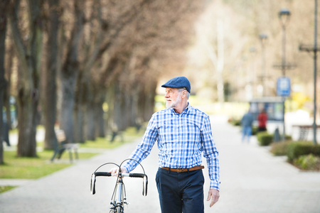 Senior man in blue checked shirt with bicycle in town.の写真素材