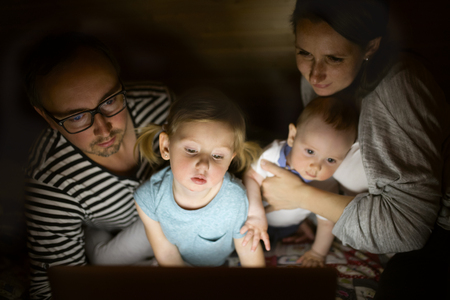 Young parents with little children and laptop at night.