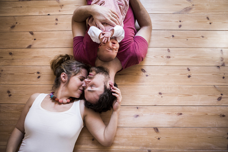 Parents holding their cute baby daughter, wooden background.の写真素材